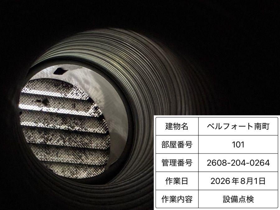 ダクトの中を写した写真。奥にある排気ガラリの細かい金網までピントが合っており、その右下に建物名・部屋番号・管理番号・作業日・作業内容を並べた看板が重なっている。